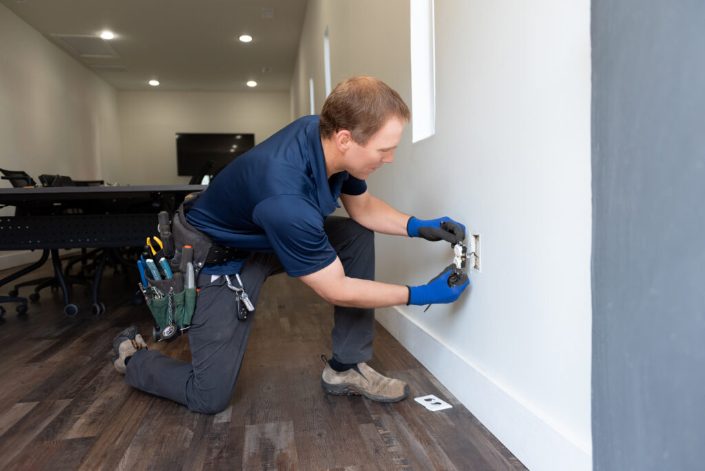 A Travis Crawford electrician completing repairs on a wall outlet in Charlotte, NC