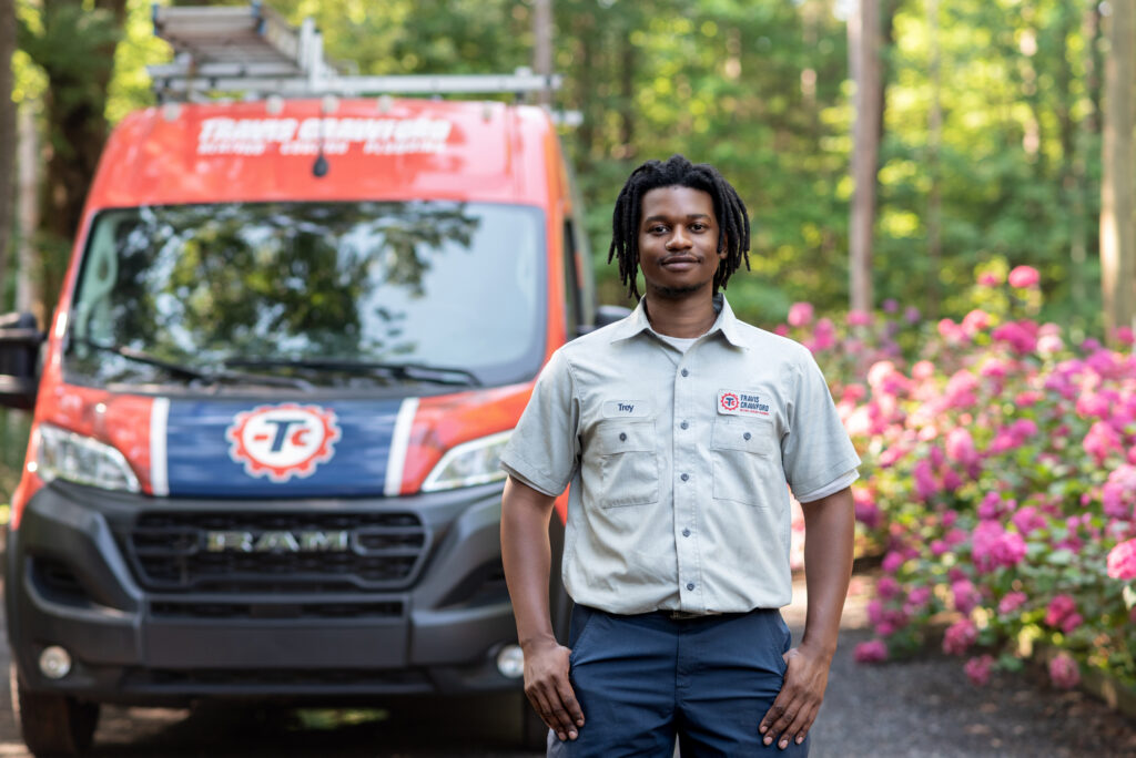 a plumber from Travis Crawford standing in front of a branded service vehicle at a Charlotte, NC home, ready to perform water line services