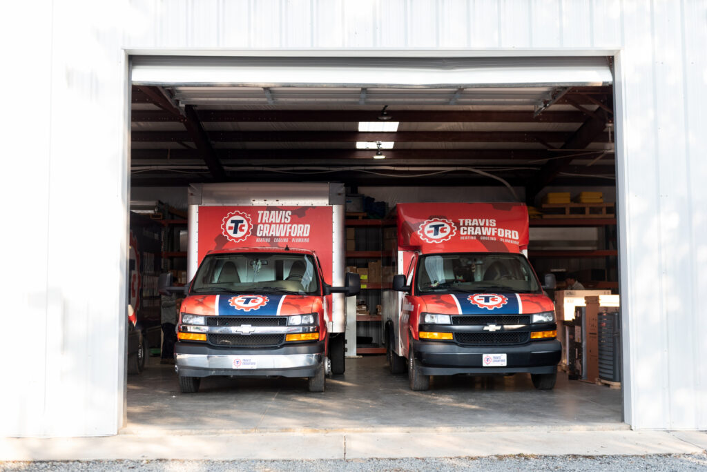 two Travis Crawford branded trucks parked in their warehouse, waiting to respond to heating emergencies in Charlotte, NC